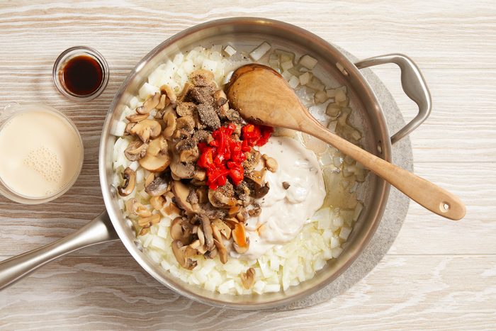 condensed soup, mushrooms, milk, pimientos, soy sauce, black pepper and hot pepper sauce being cooked with onions in melted butter