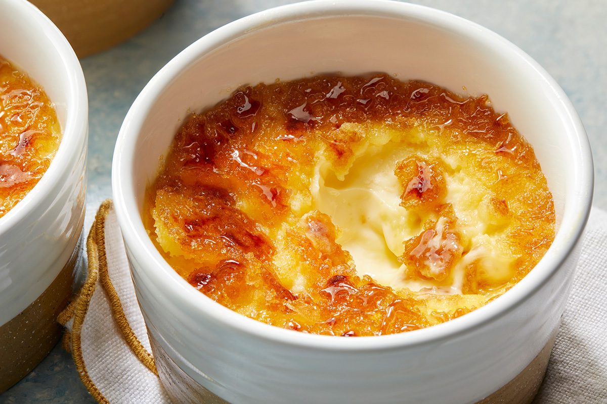 A close-up of creamy crème brûlée in a white ramekin, with a golden caramelized sugar crust on top.