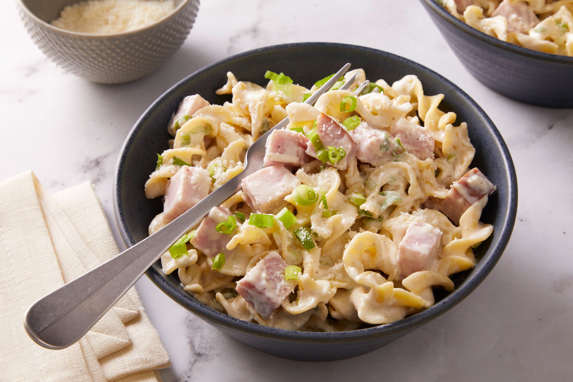 Top Down view of a single bowl of Hurry-Up Ham N Noodles, placed between small dishes of cheese.
