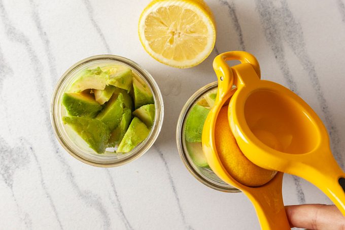 Avacados placed in a jar and lemon is squeezing in one jar