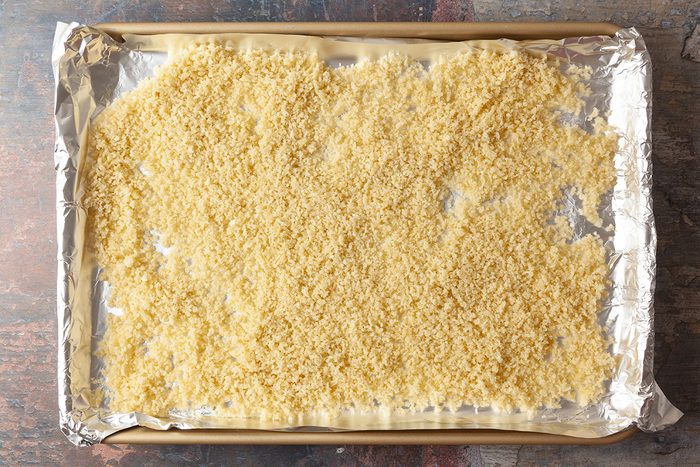 A baking sheet lined with foil is covered with an even layer of uncooked orzo pasta spread out across the surface.