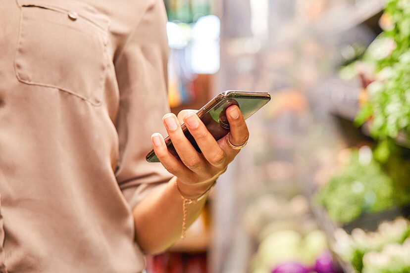Woman checking her shopping list on her phone in a supermarket