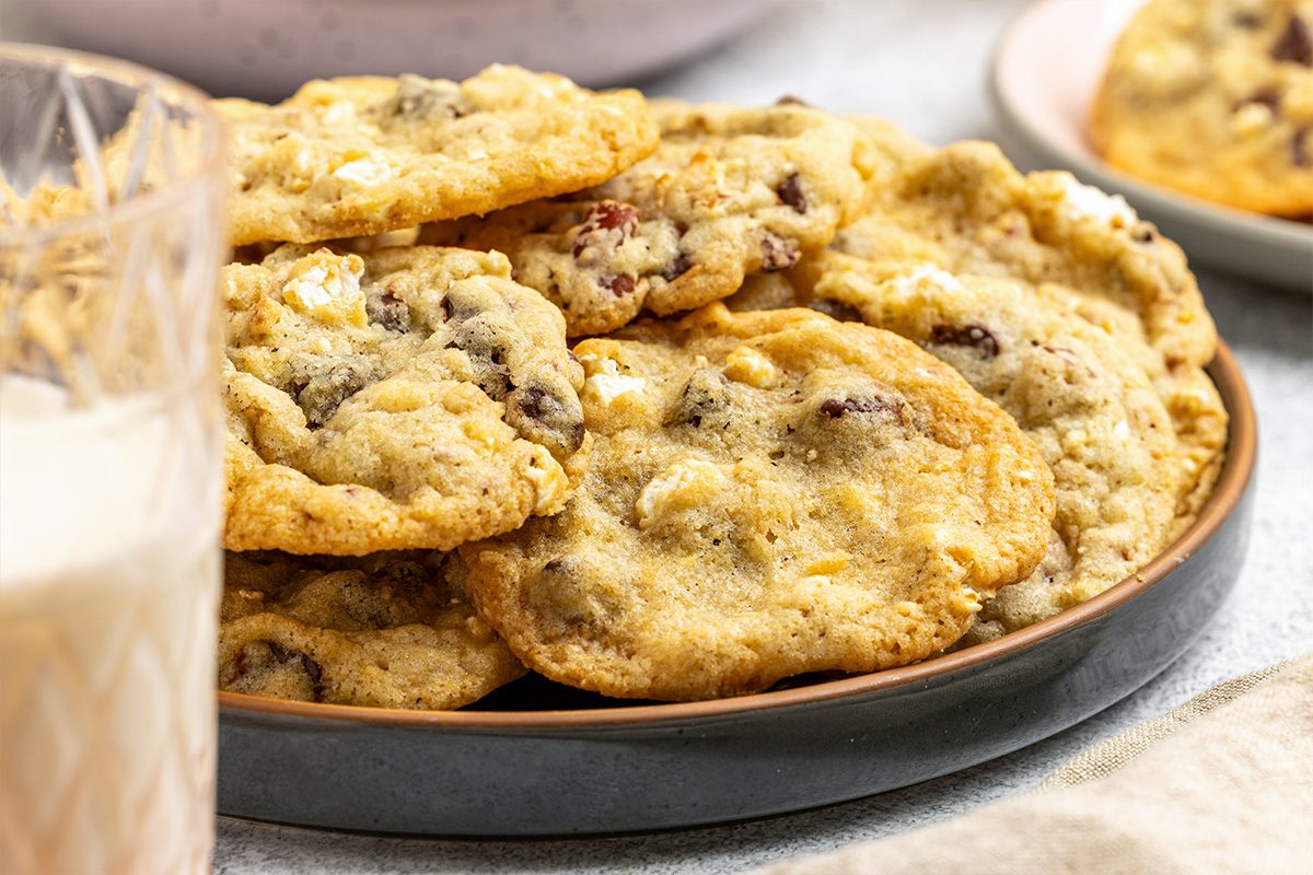 A plate of homemade cookies with chocolate chips and nuts sits on a table next to a glass of milk.