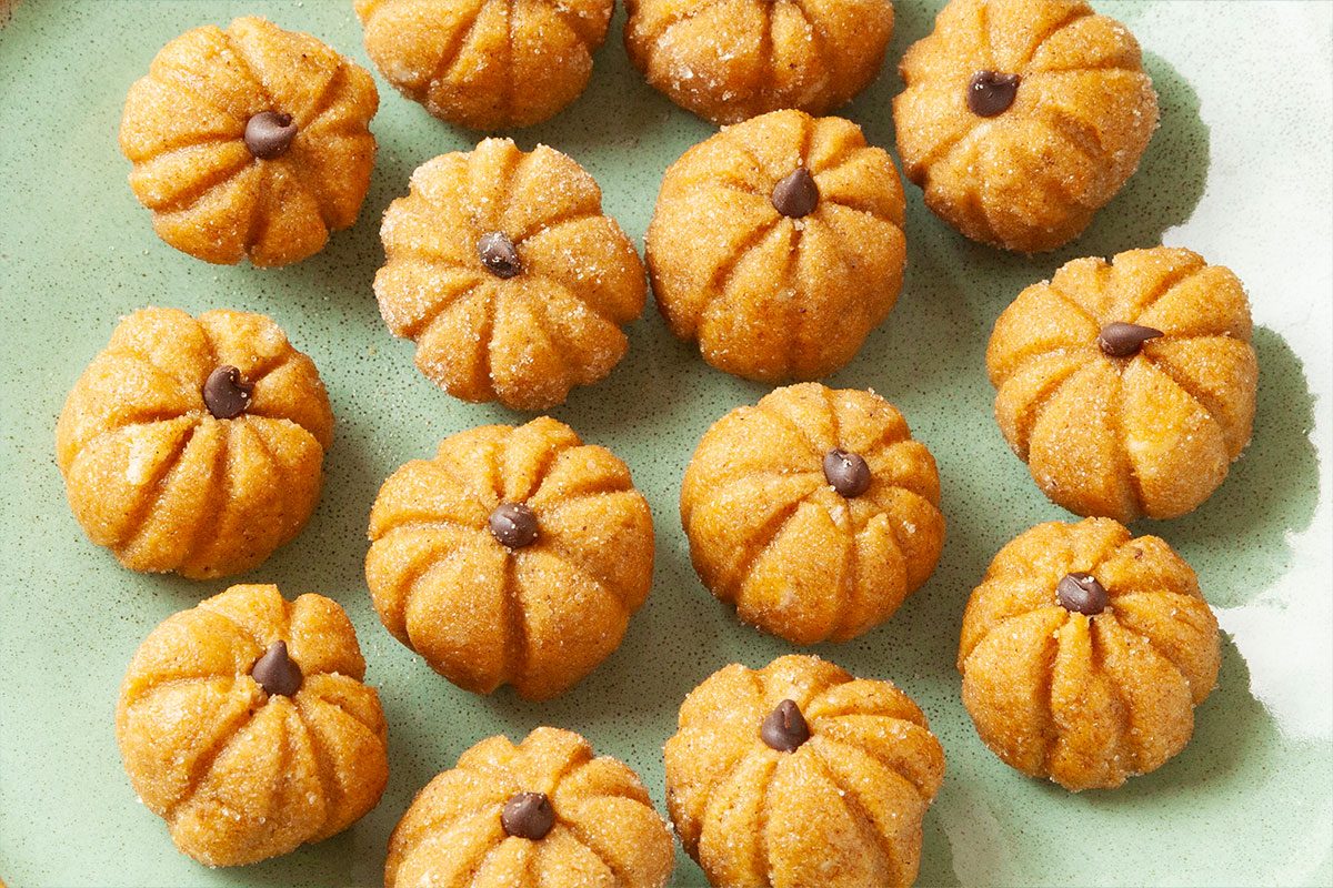Small, pumpkin-shaped cookies with a sugar coating and a chocolate chip in the center, arranged on a green plate.