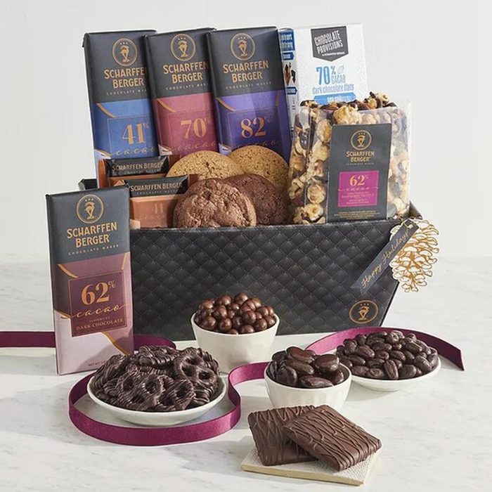 A gift basket filled with Scharffen Berger chocolate bars, cookies, chocolate-covered pretzels, popcorn, and assorted chocolate treats displayed on a table with a purple ribbon.