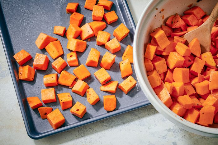 seasoned potatoes on a greased 15x10x1-inch baking pan next to a bowl with potato cubes