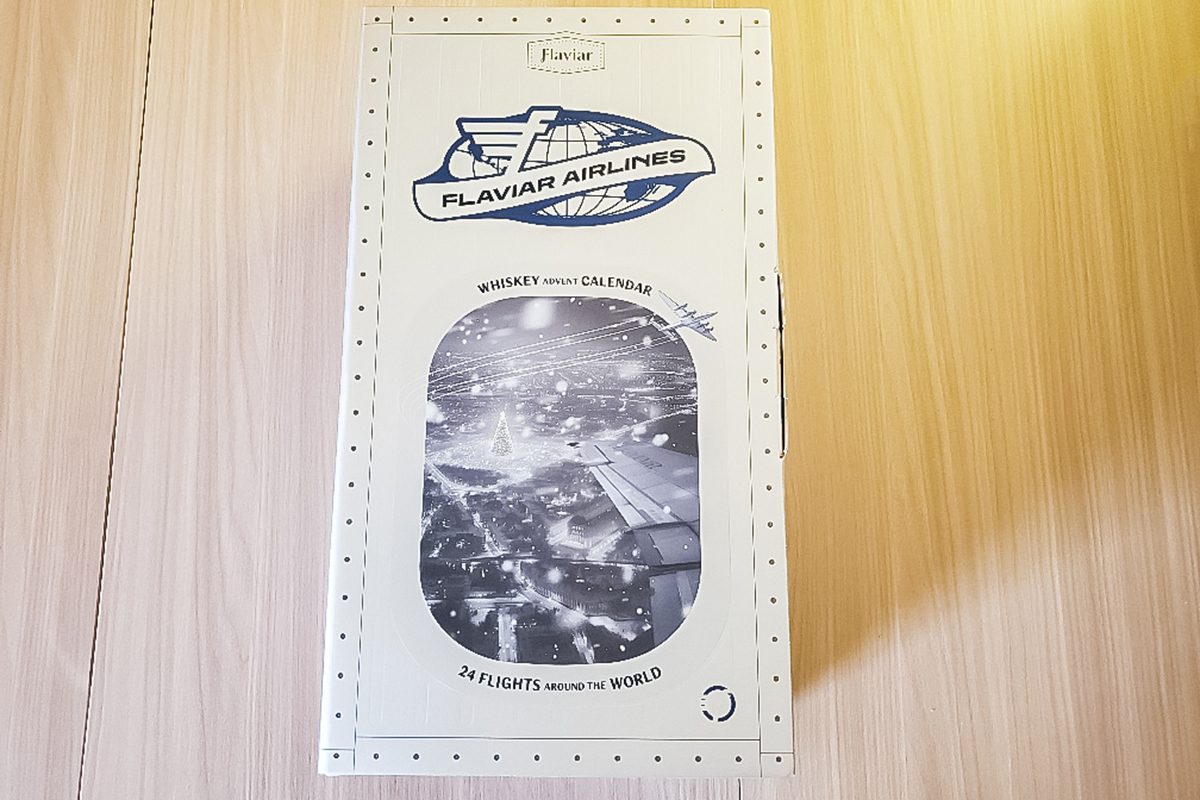 A rectangular menu or pamphlet from Flaviar Airlines featuring a logo with an airplane, a black-and-white photo of an airport at night, and decorative dotted borders, placed on a light wooden surface.