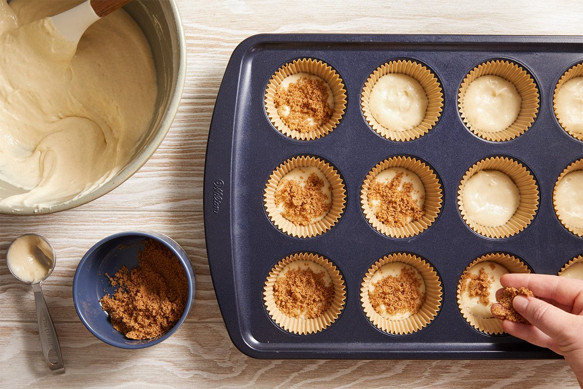 Overhead view of a muffin tin filled with smooth batter Top each with cinnamon sugar mixture, plated neatly for baking