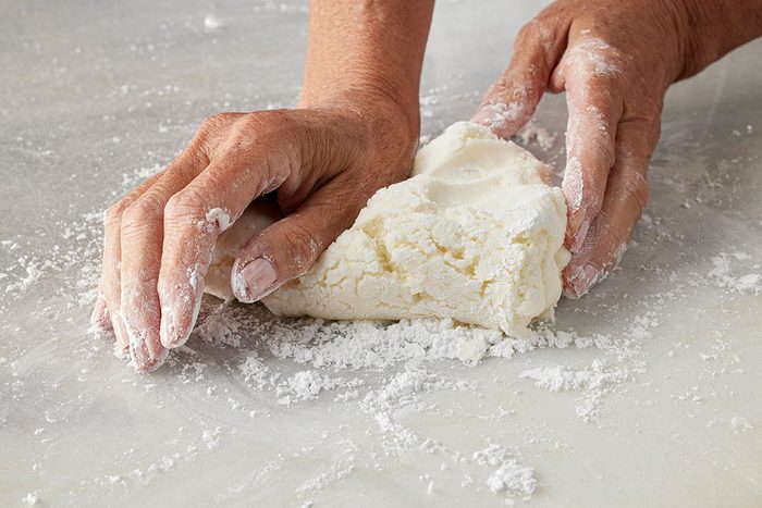 Close-up shot of hands kneading a mound of dough on a floured surface;