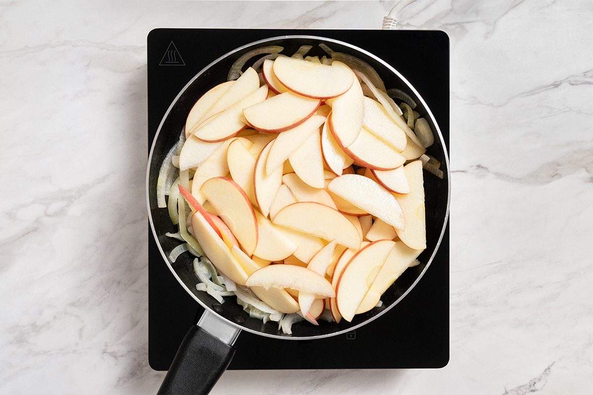 Overhead shot of placing apples on top of onions; induction; all set on a marble surface;
