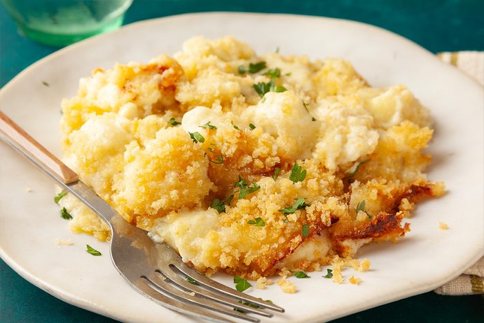 Close-up shot of a white plate with creamy Gnocchi Mac and Cheese topped with golden breadcrumbs and parsley, with a fork on the side