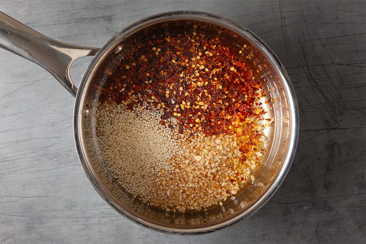 Overhead shot of oil simmering in a saucepan with crushed red pepper flakes and spices starting to infuse.