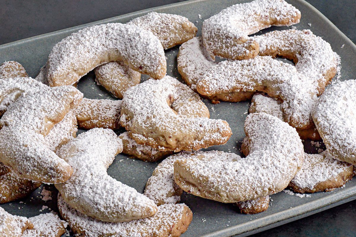 3/4th Shot of Pecan Crescent Cookies; A platter shows crescent-shaped cookies covered in powdered sugar arranged neatly on a rectangular plate they slightly overlap each other