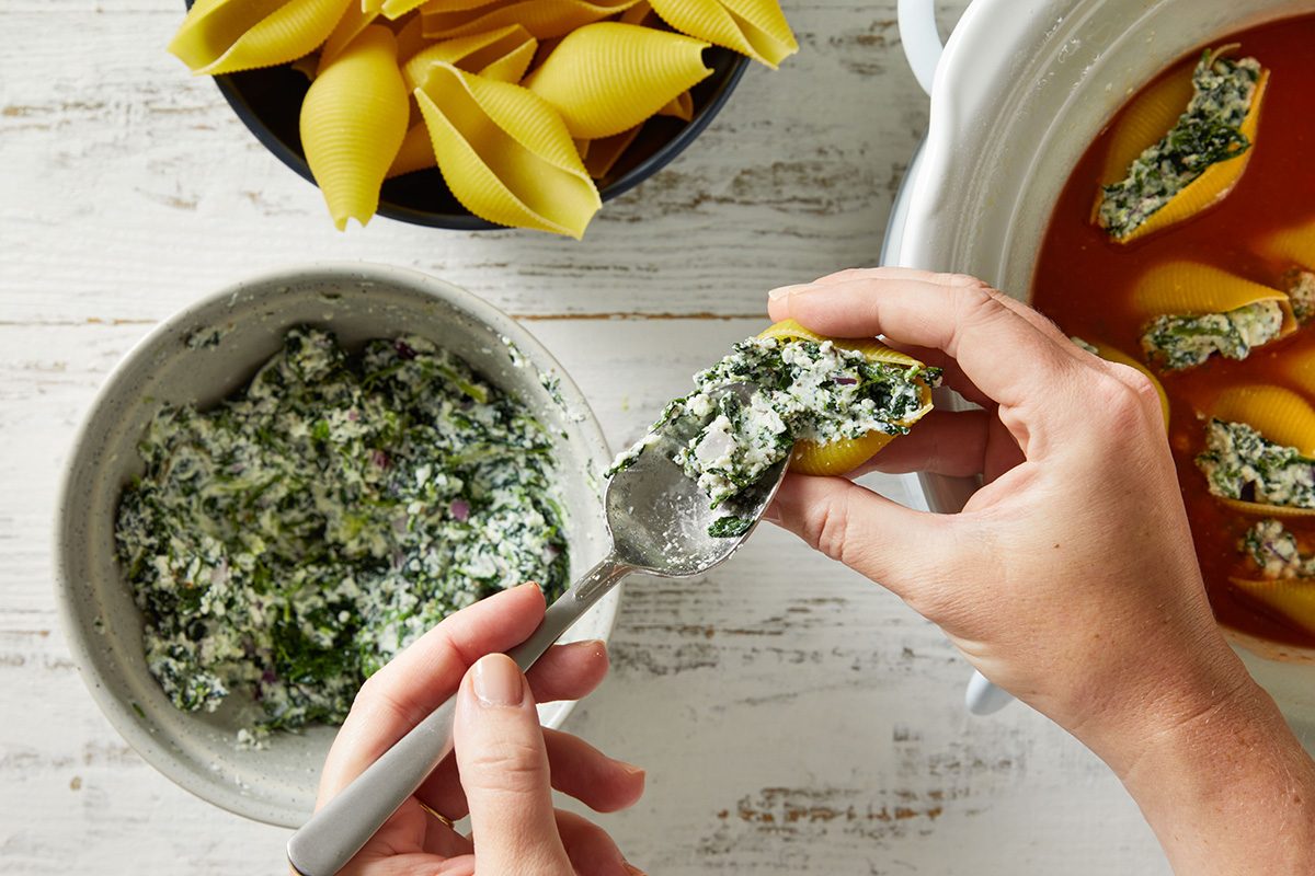 Overhead shot of a hand stuffing pasta shells with the ricotta-spinach mixture 