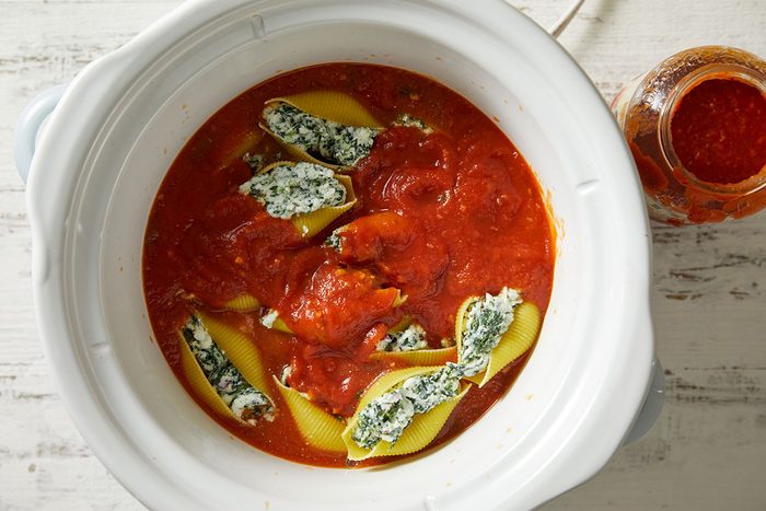 Overhead shot of stuffed pasta shells arranged neatly in a slow cooker filled with tomato sauce.