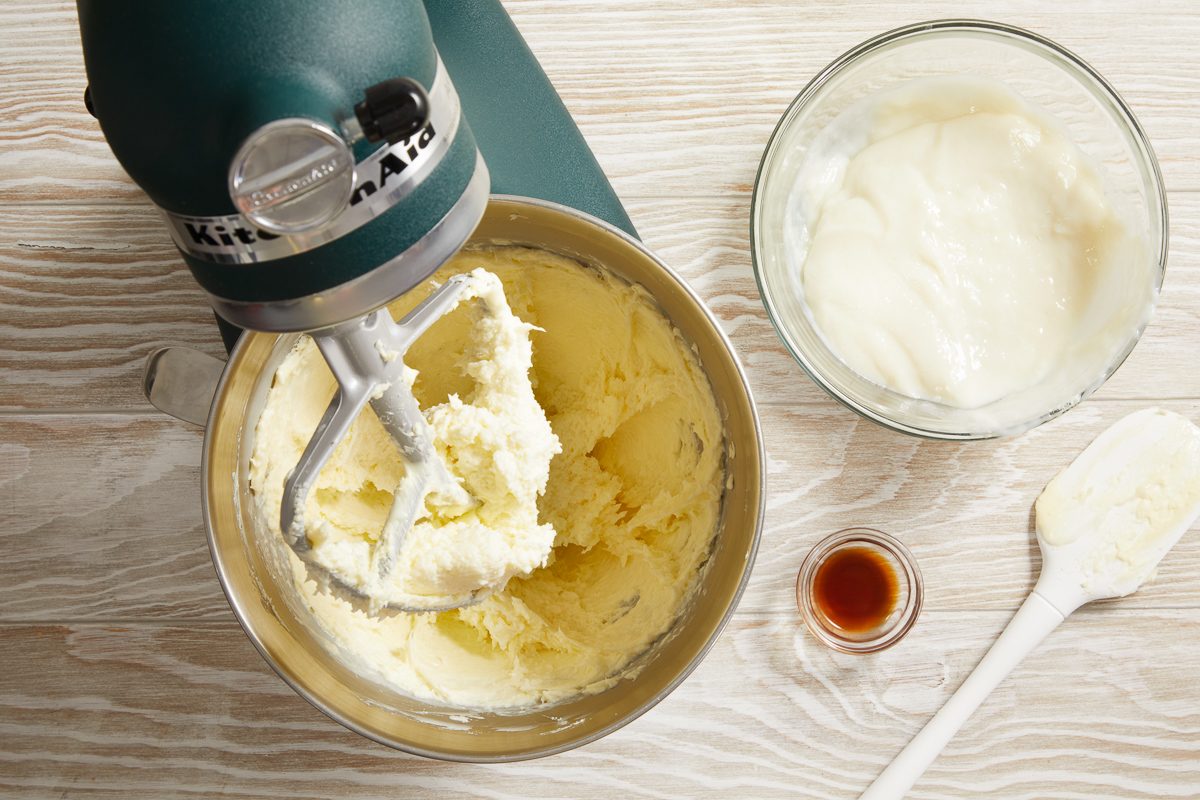 beating butter in a mixing bowl with frosting mixture next to it in another bowl