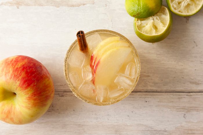 Closeup shot of a Harvest Mezcalita in a glass with ice, red apple slices, and a cinnamon stick