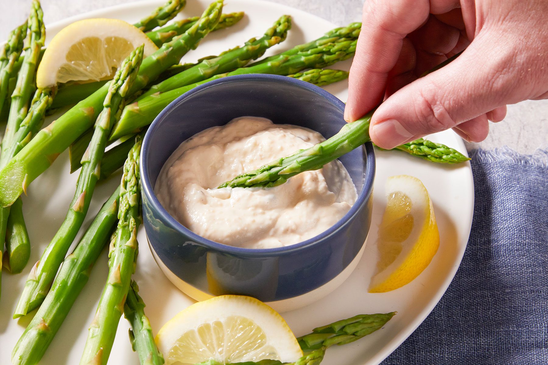 Asparagus With Horseradish Dip in plate and bowl with lemon wedges on side.