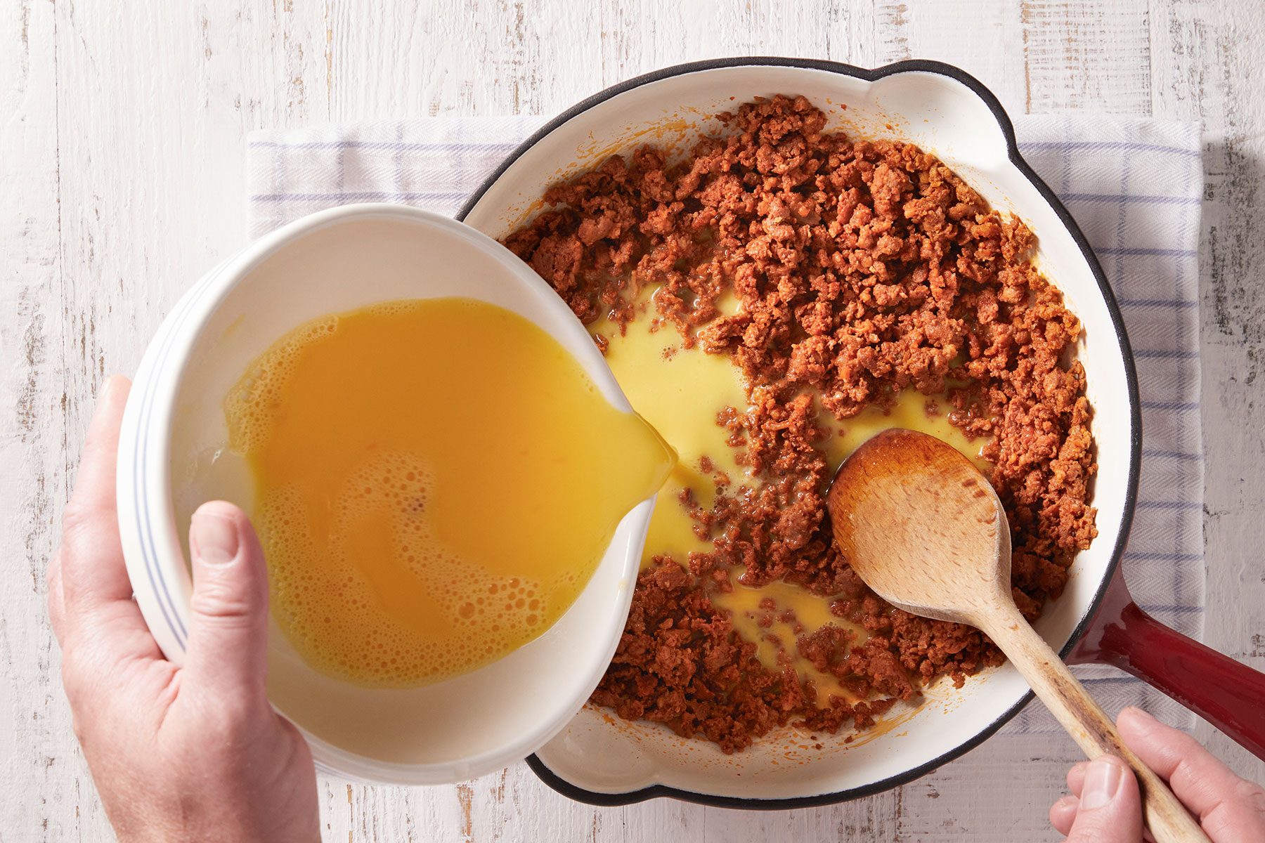 Adding egg mixture to the chorizo in a heavy skillet with a ladle continuously stirring it.