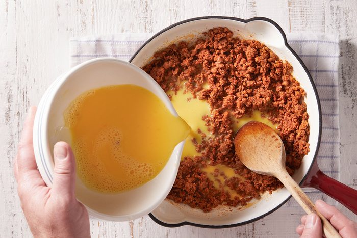 Adding egg mixture to the chorizo in a heavy skillet with a ladle continuously stirring it.