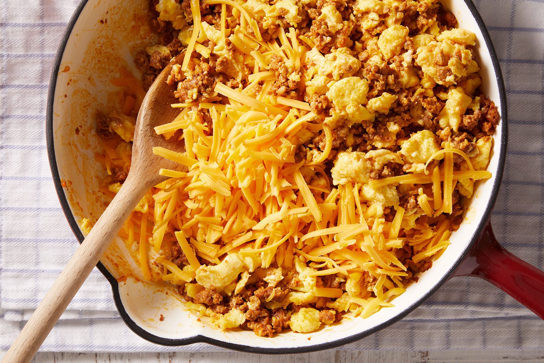 Stirring in cheese to the Chorizo in a large skillet with a ladle to mix it.