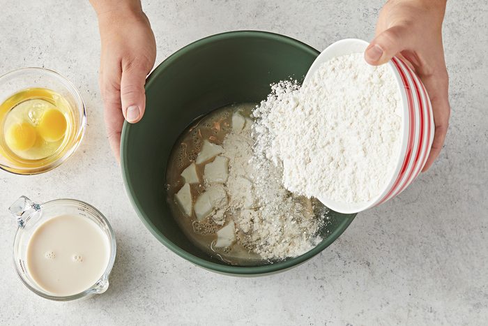 Adding evaporated milk, sugar, shortening, salt, eggs and 2 cups of flour into the large bowl with the yeast mixture.