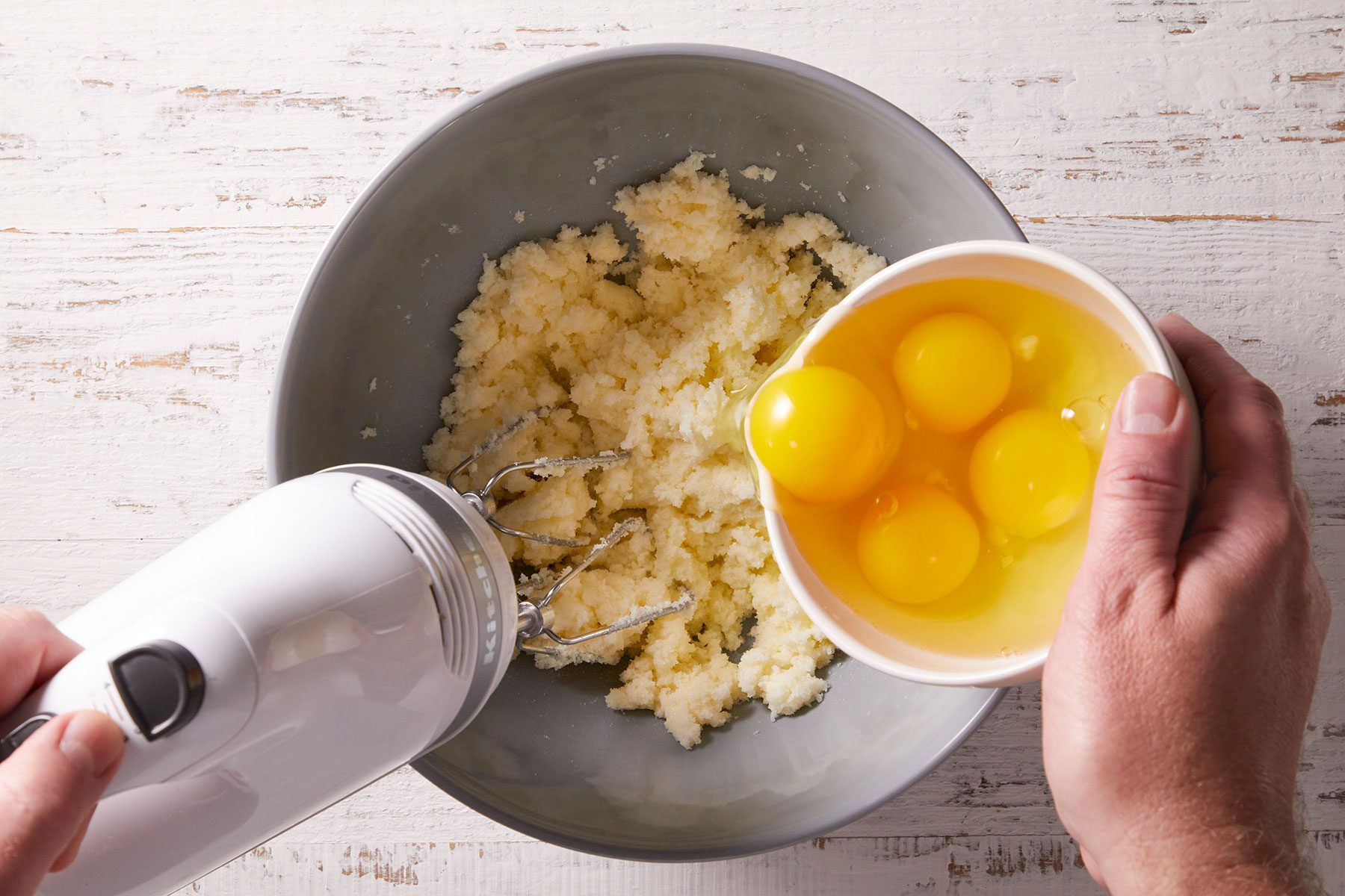Beating eggs into butter and sugar mixture in a bowl to bake a cake.