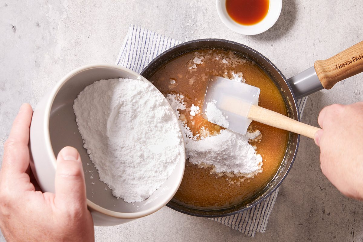 Overhead shot of icing sugar being stirred into a saucepan to prepare frosting.