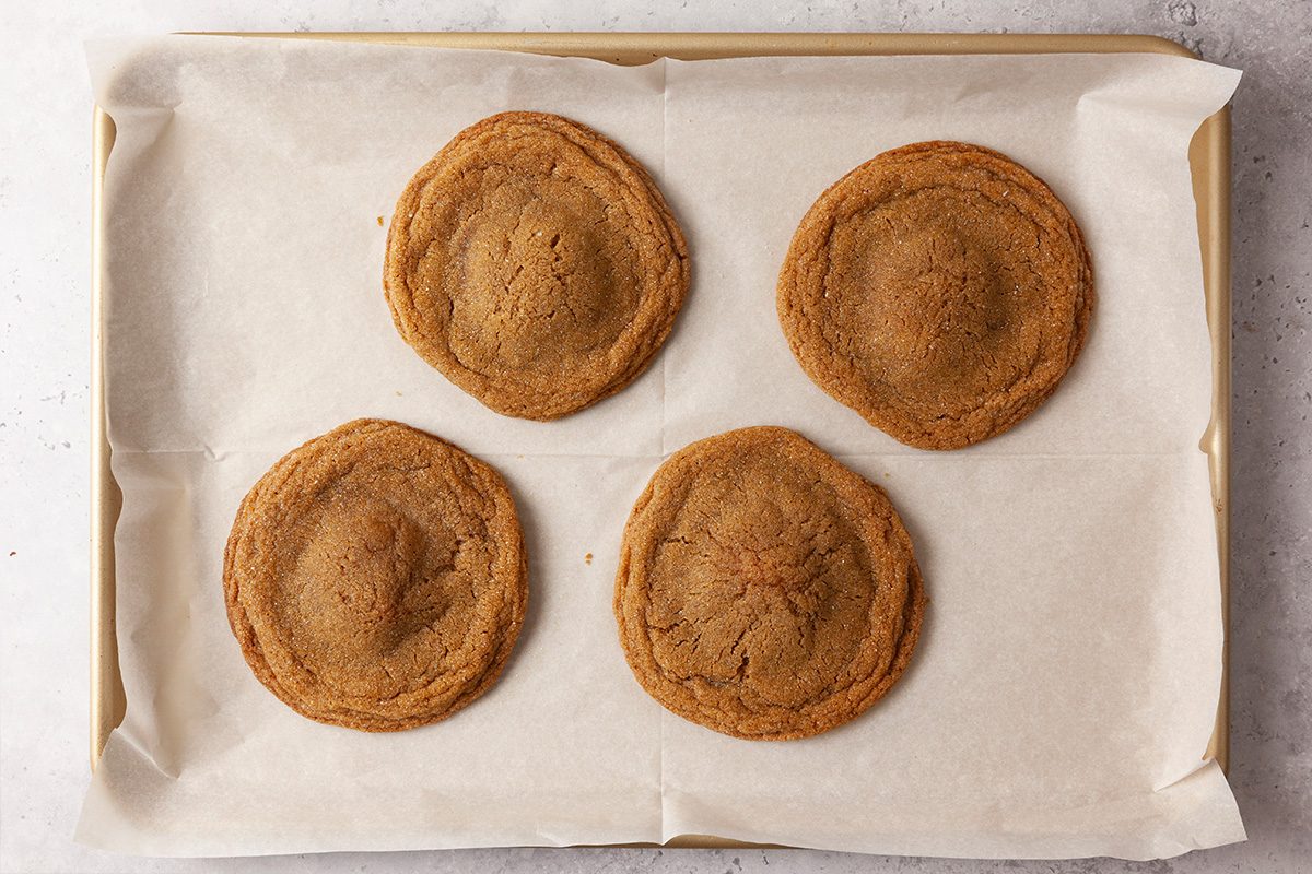 Overhead shot of four large, round cookies with raised centers arranged evenly on a parchment-lined baking sheet; The cookies are golden brown and look freshly baked, spaced in a neat grid pattern;