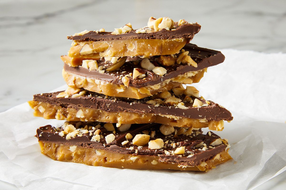 Close-up of stacked layers of Hazelnut Toffee showing glossy chocolate coating and crunchy nut topping.
