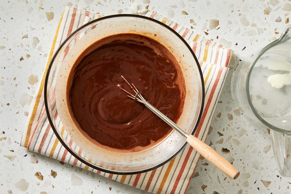 Overhead view of a mixing bowl filled with smooth chocolate batter and a spatula resting inside on a terrazzo countertop.