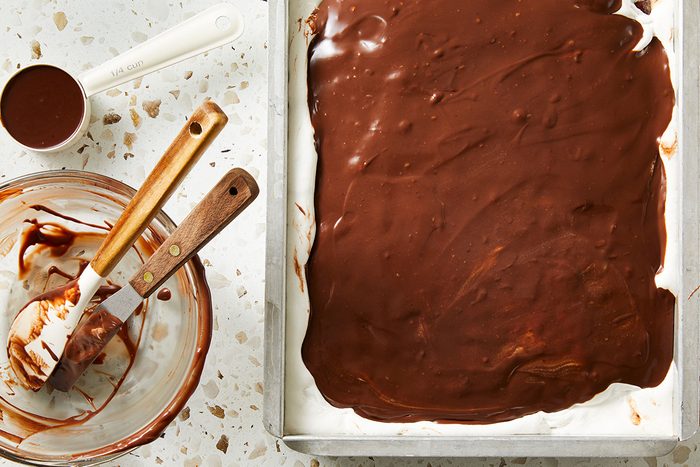 Overhead shot of the cake evenly spread with smooth chocolate frosting, surrounded by mixing bowls and spatulas coated in chocolate.