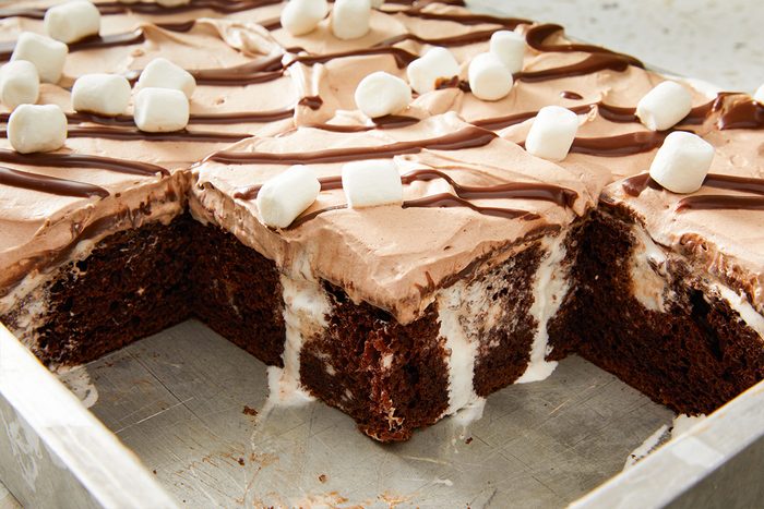 Close up shot of the Hot Chocolate Poke Cake in the pan, topped with chocolate drizzle and marshmallows, with one large slice taken out.