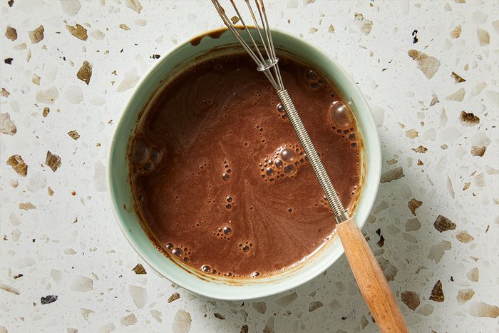 Top-down shot of glossy chocolate pudding mixture in a small bowl with a whisk resting on the edge.