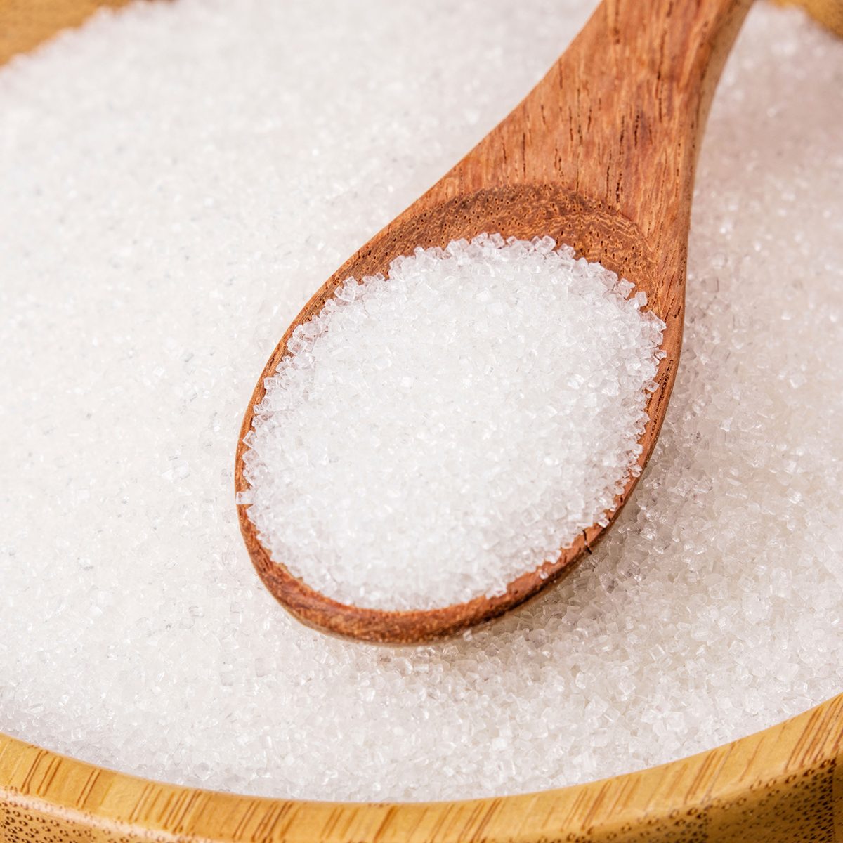 Wooden bowl full of granulated sugar with a wooden spoon on a wooden background