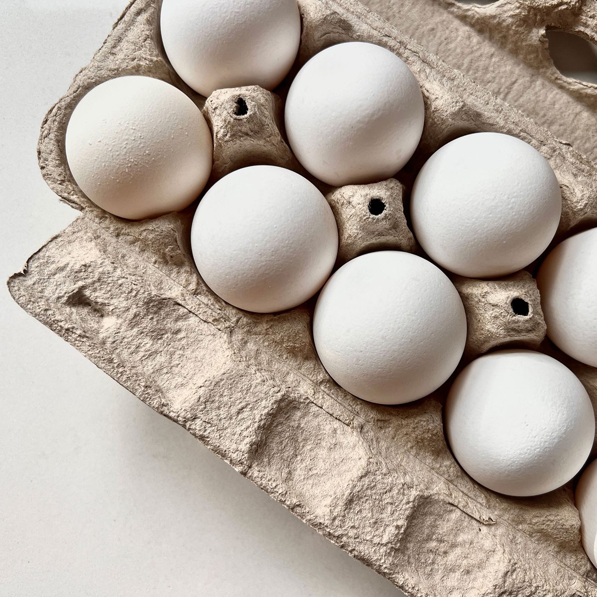 A carton of 12 fresh eggs rests on a rustic wooden table, showcasing their natural colors and farm-fresh quality.