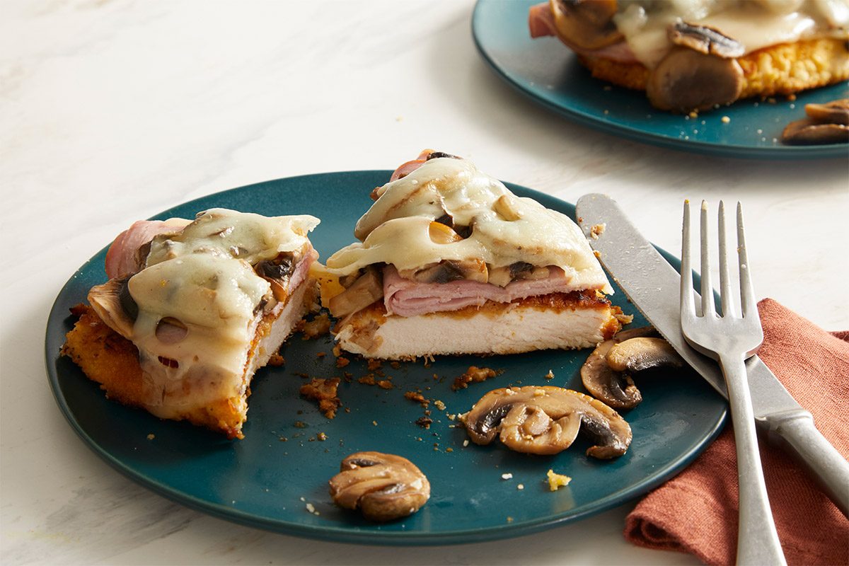 Overhead shot of plated Swiss Mushroom Chicken with melted cheese and mushrooms served on a blue plate with a fork and napkin.
