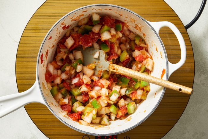 onions, bell peppers, diced tomatoes, picante sauce, garlic and cumin being combined in a saucepan