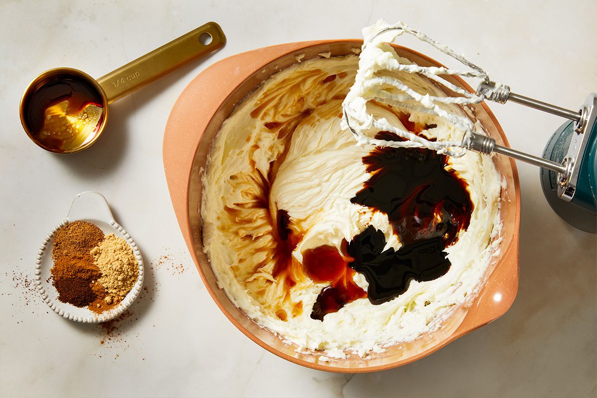Overhead shot of cream cheese mixture in a mixing bowl being blended with molasses and spices, beaters coated with the rich gingerbread filling.