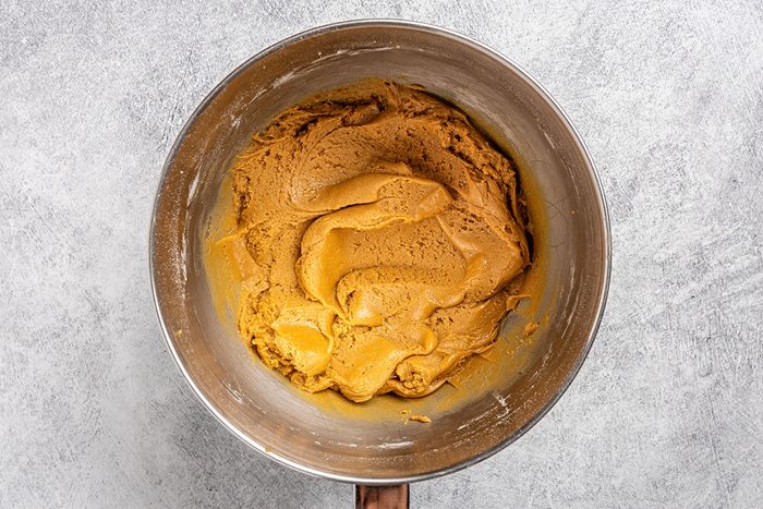 Overhead shot of a stainless steel mixing bowl filled with light brown cookie dough; resting on a light gray countertop.